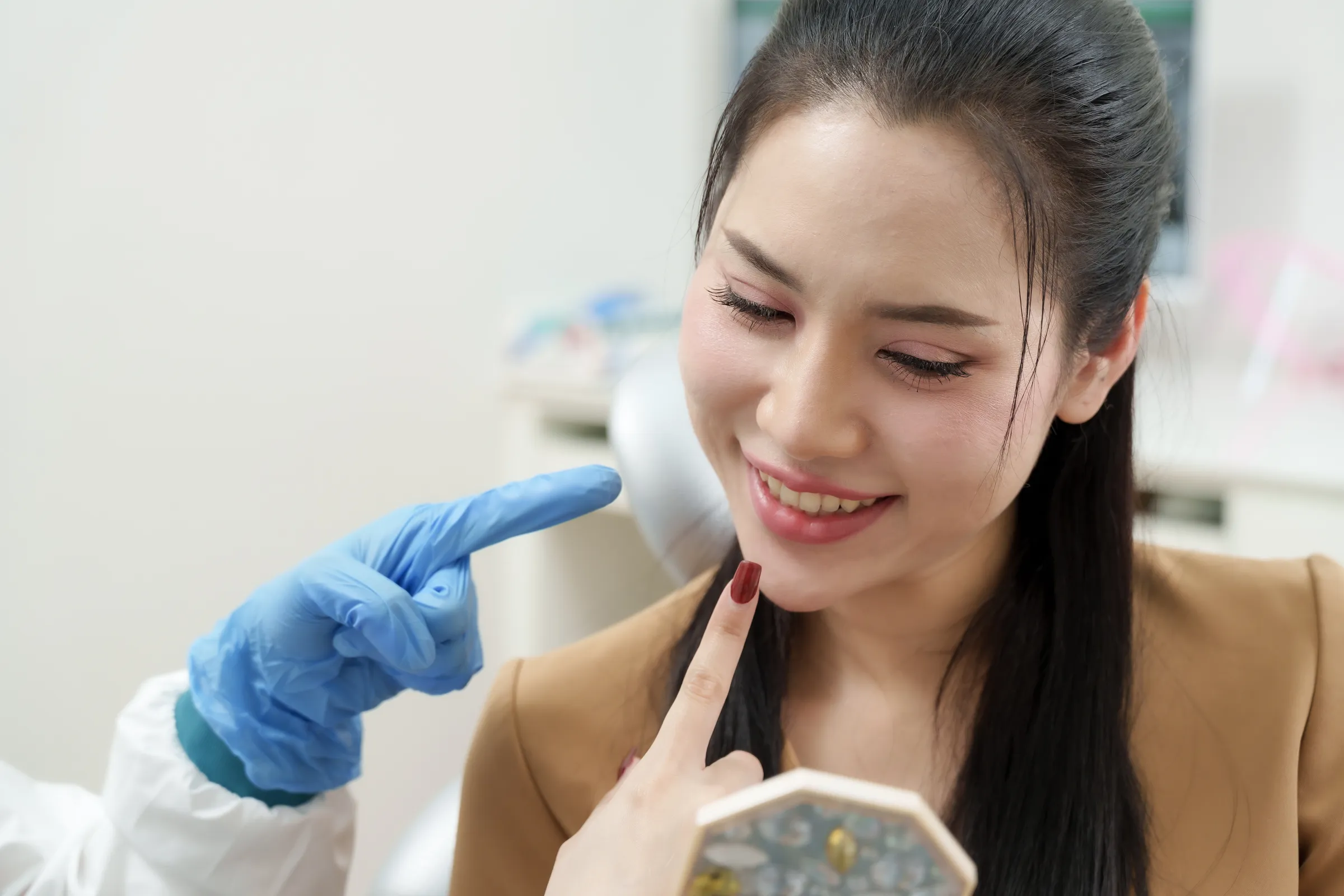A dentist pointing to a model of the gums while a patient touches her lip