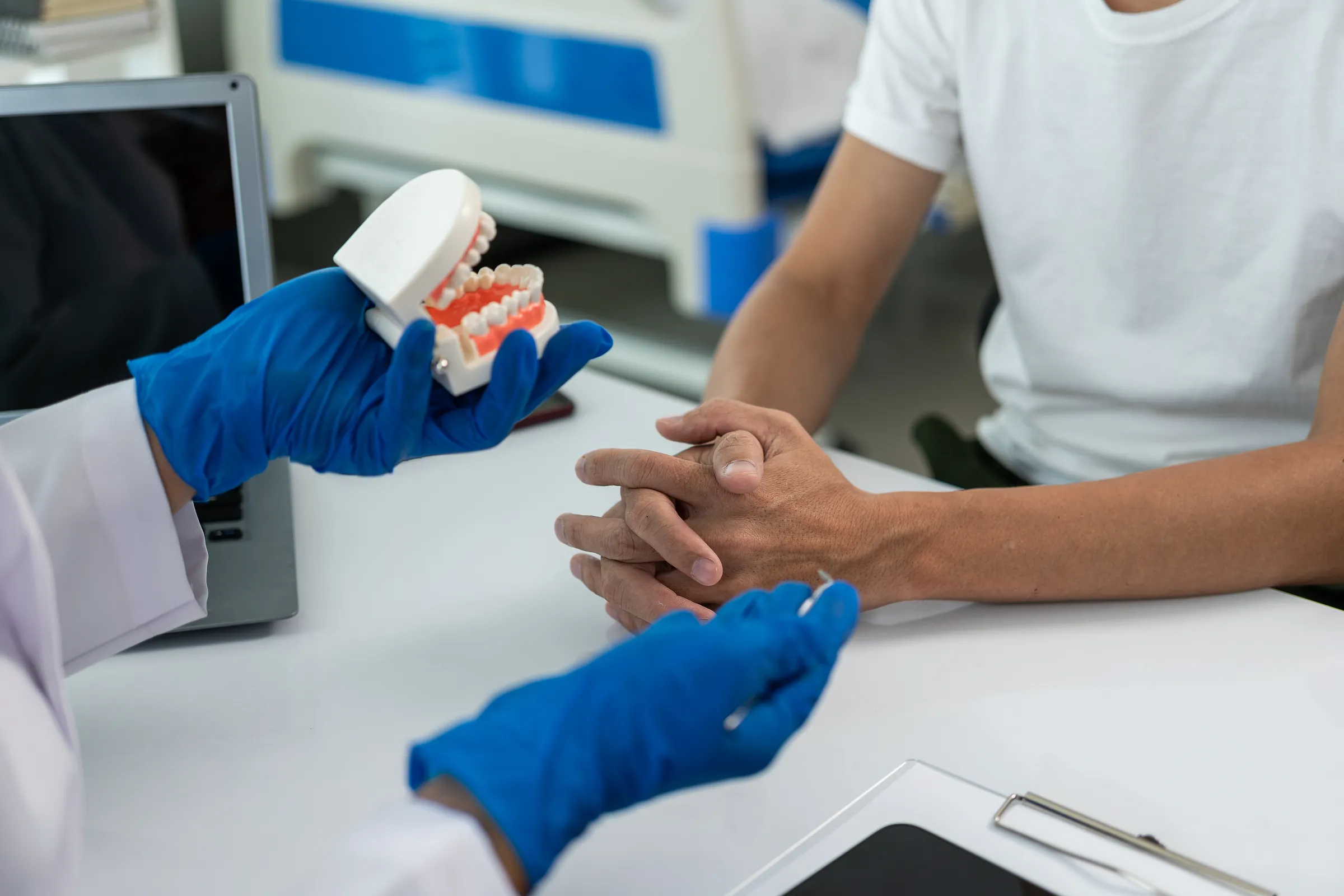 A dentist holding a denture while talking with a patient at a desk