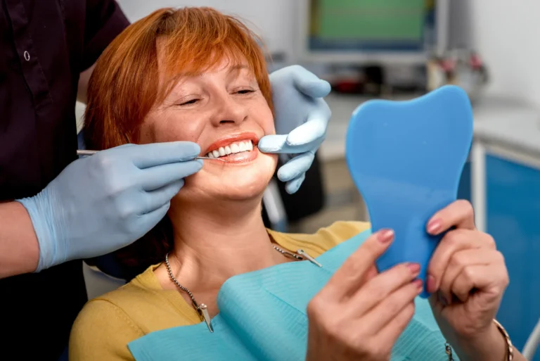 A smiling woman checking her teeth in a hand mirror at the dentist