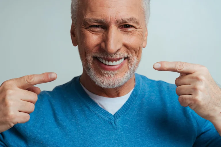 A smiling older man pointing to his teeth