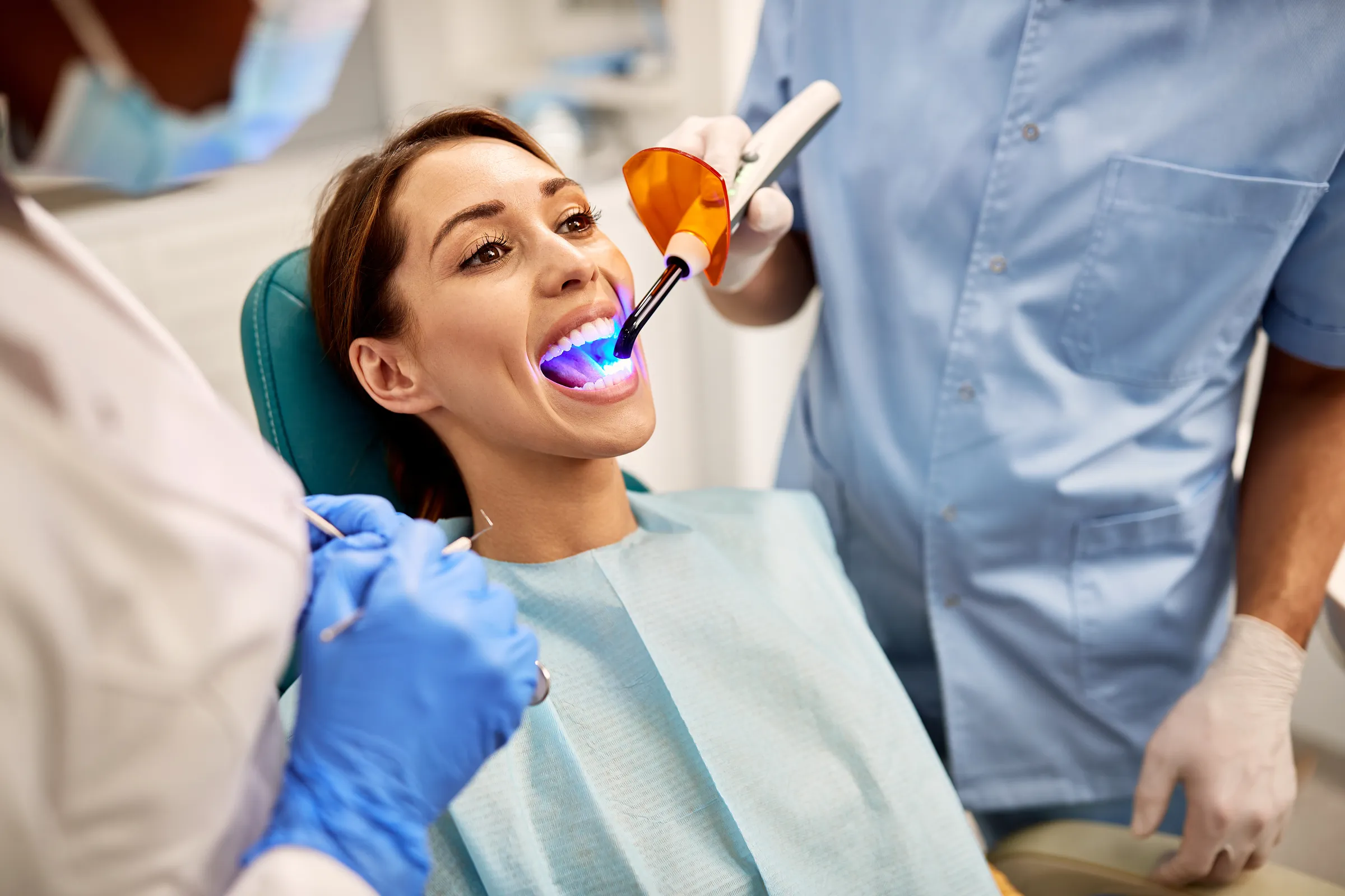 A patient in the dental chair while a curing light hardens a tooth-colored filling