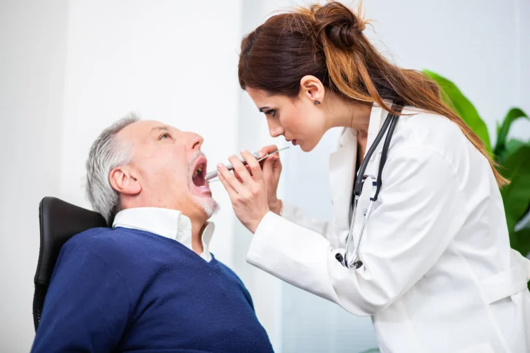 Dentist examining an older man’s mouth with a dental mirror during an oral cancer screening
