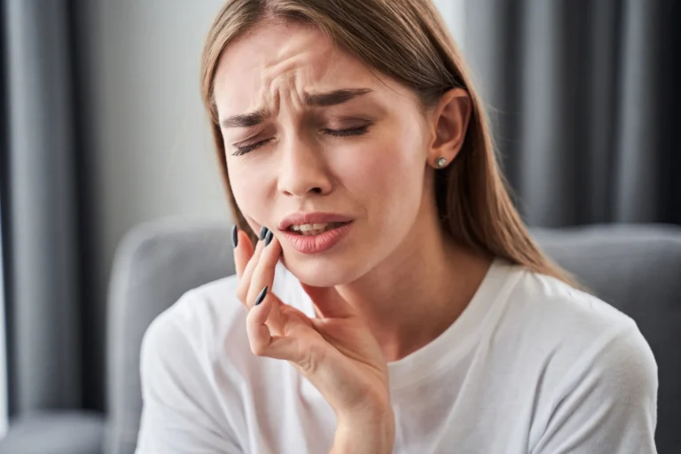 A young woman holding her cheek in pain from a wisdom tooth