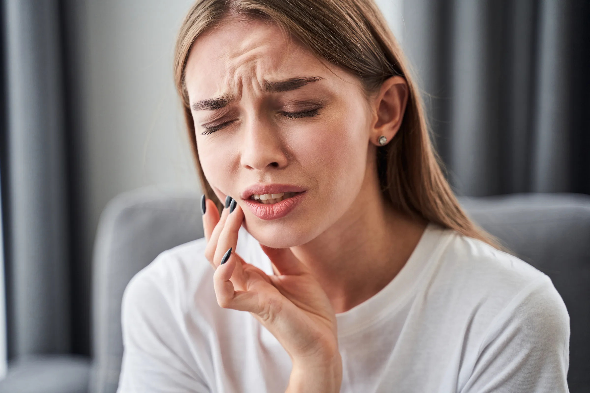 A young woman holding her cheek in pain from a wisdom tooth