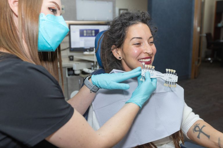 A team member holding a shade guide up to a smiling patient’s teeth