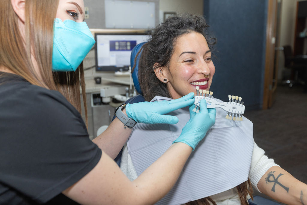 A team member holding a shade guide up to a smiling patient’s teeth