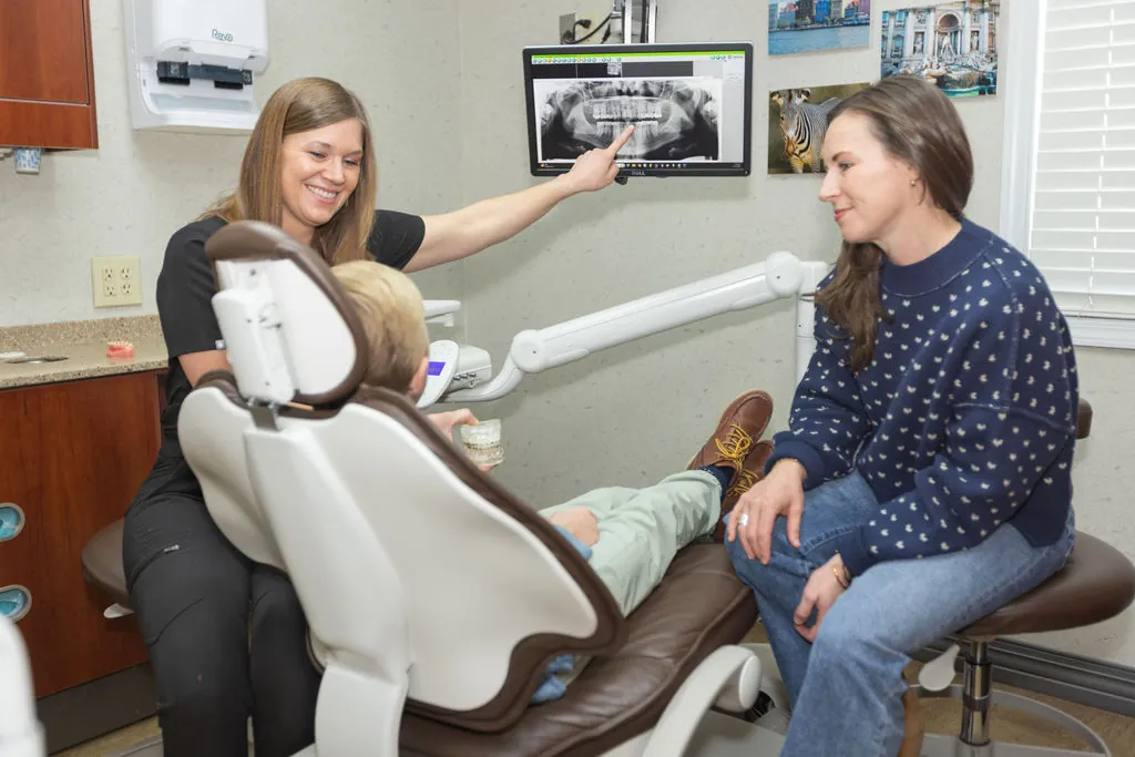 A dentist showing a patient and parent an X-ray on screen