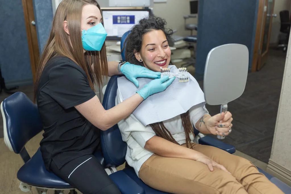 A team member checking a patient's smile with a shade guide