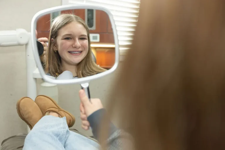 A young patient with braces smiling into a hand mirror